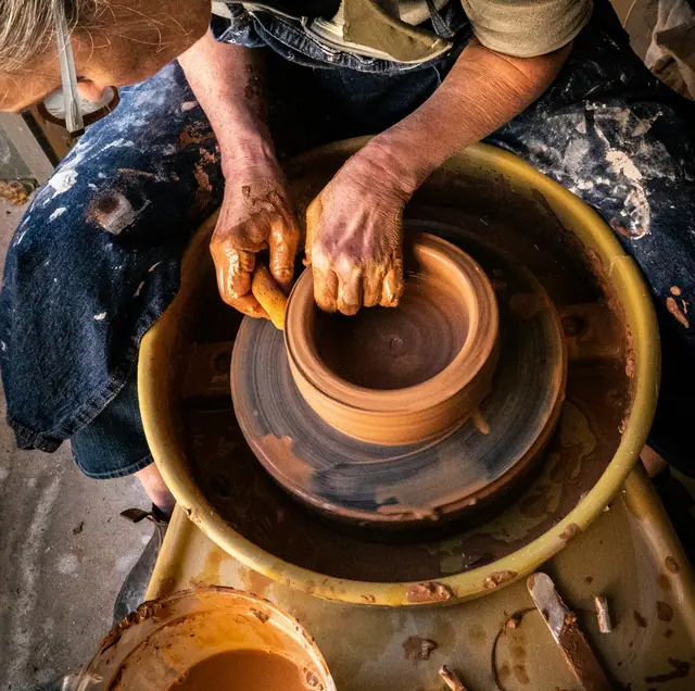 Mãos puxando uma peça de barro no torno