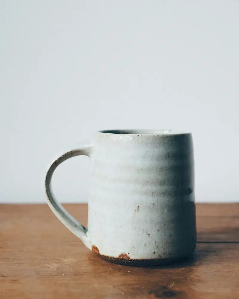 Caneca cinza-clara com alça larga sobre mesa de madeira