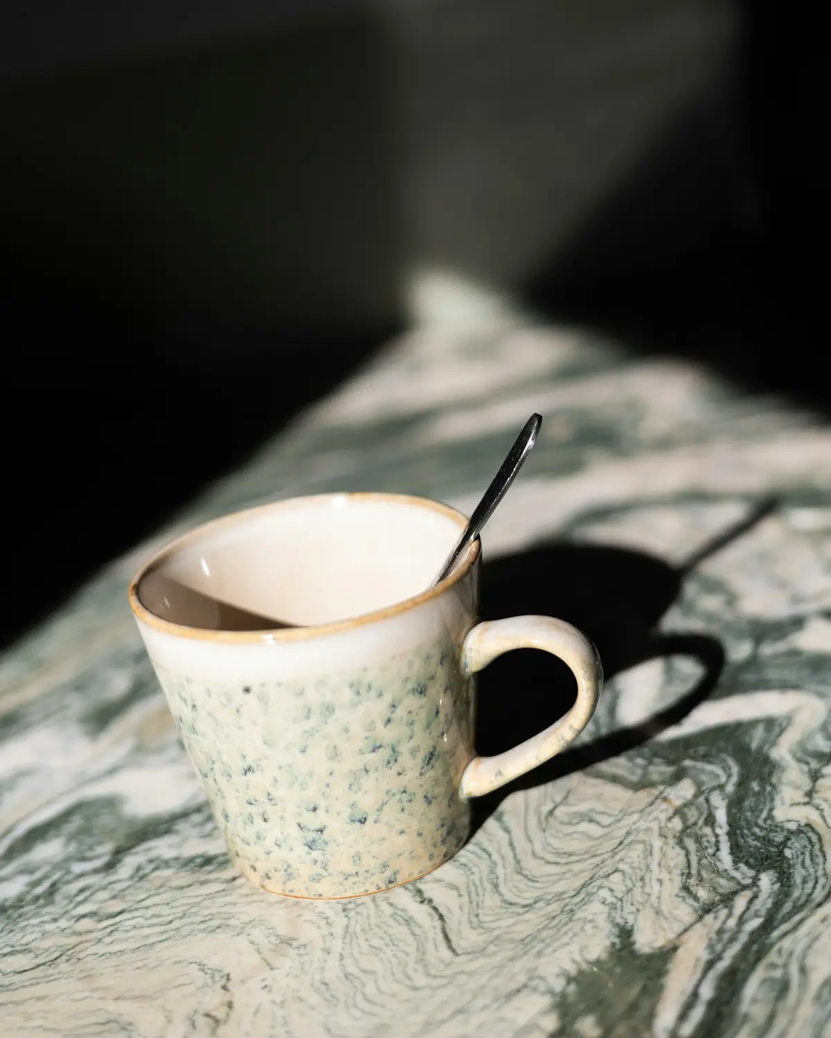 Caneca branca salpicada de verde, com colher, sobre pedra verde