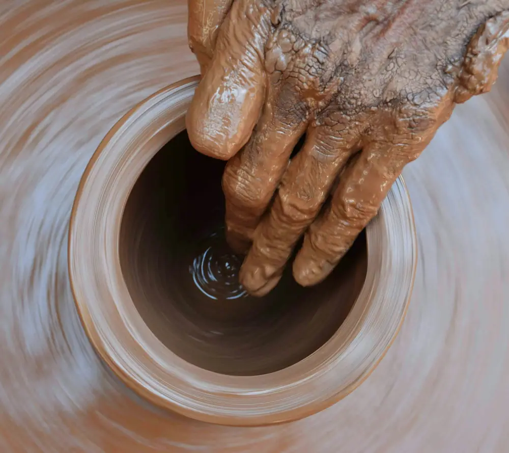 Mão dentro de uma peça girando no torno, o barro em espiral